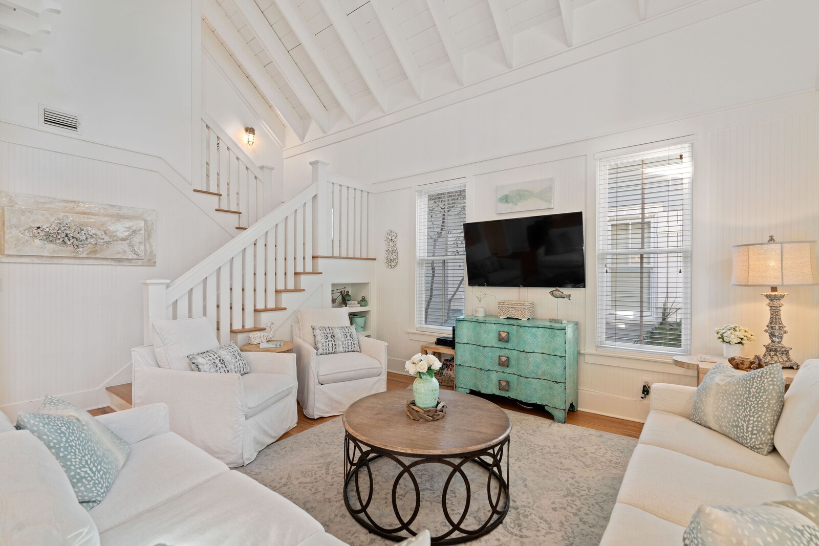 Open living room with vaulted ceiling, white seating, and staircase